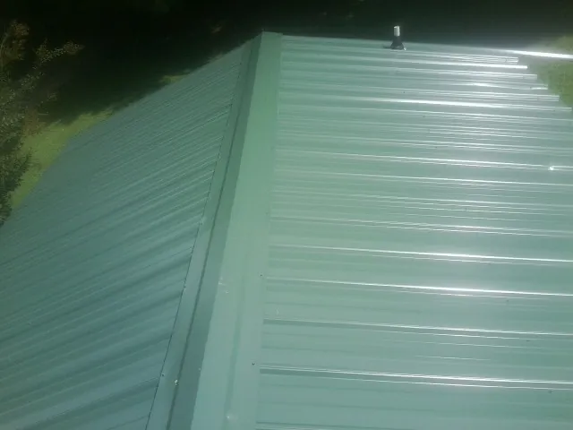 New green metal panels meeting at the ridge of a roof — Flat Roof Repair work by our crew in Holt