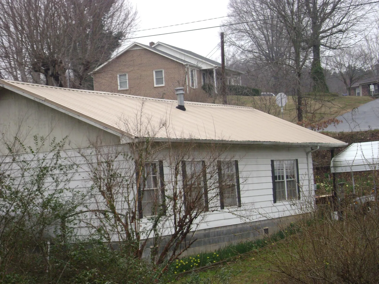 Tan metal roof on a white sided house set into a hillside — Commercial Roofing by Roofing Brothers in Holt