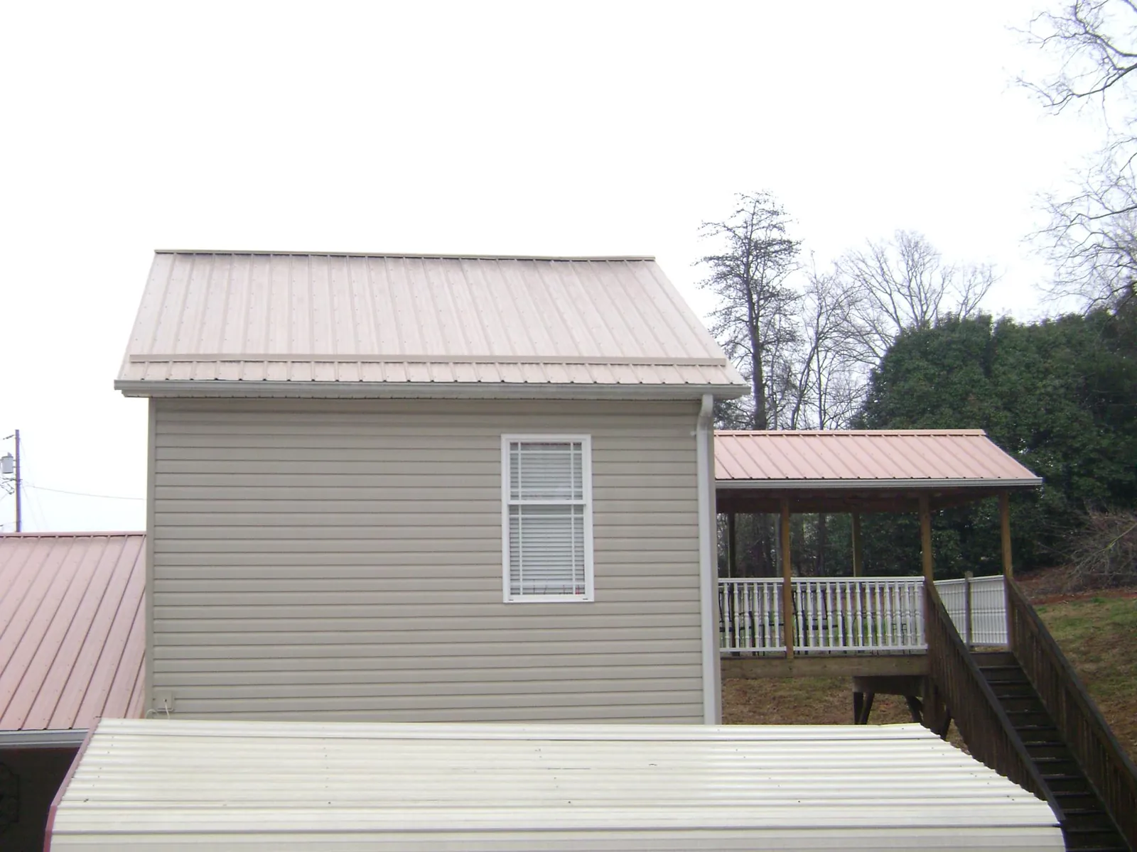 Tan metal roofs on a two story addition and attached porch in Holt
